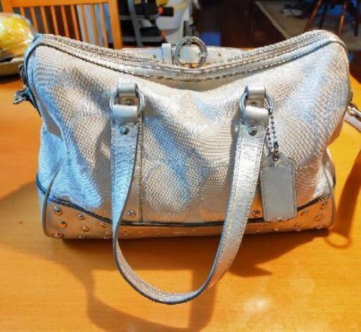 ホワイトとシルバーが素敵なCOACH（コーチ）\n\nシグネチャーキャンバスを採用したエレガントな雰囲気漂う一品。底マチの広いボストンバッグは型崩れしにくく、荷物をたっぷり収納することができます。床に置いても汚れにくい底鋲付き